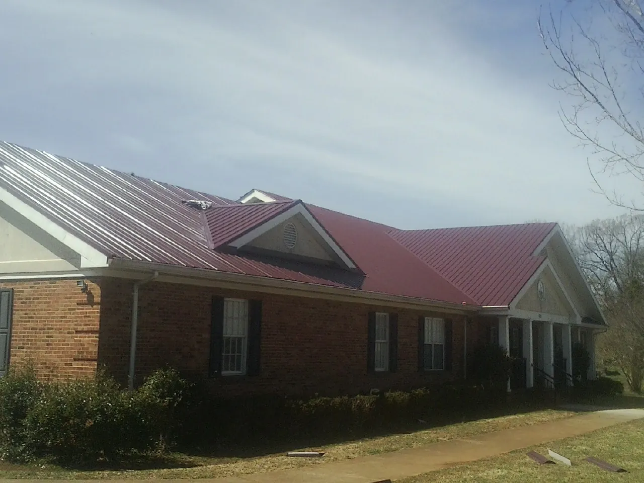 Red metal roof with gabled entries on a long brick building, from a Hail Damage Roof Repair job in Amherst