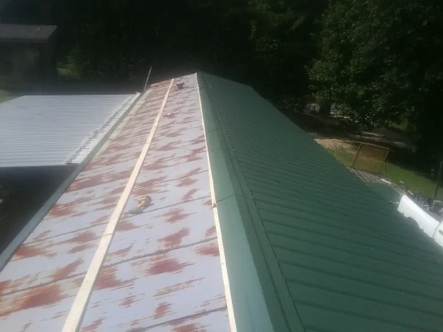 Old rusted panels beside newly installed green metal roofing — Wind Damage Roof Repair by Roofing Brothers in Amherst