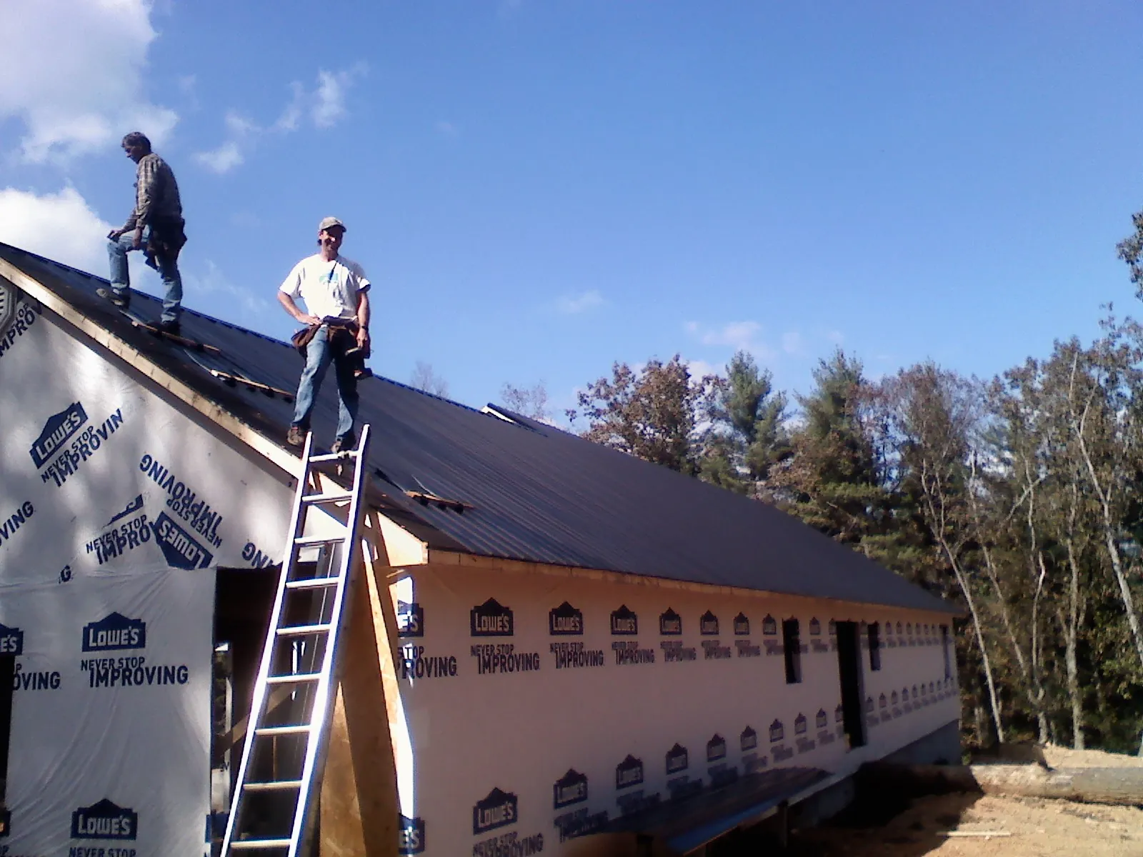 Two roofers standing on a long dark metal roof over a wrapped building in Amherst