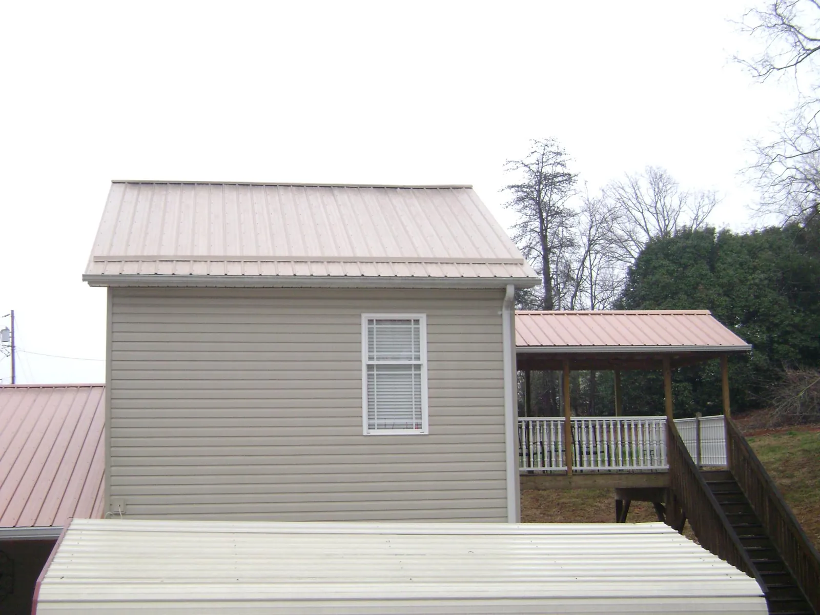 Tan metal roofs on a two story addition and attached porch, from a Roof Replacement job in Amherst